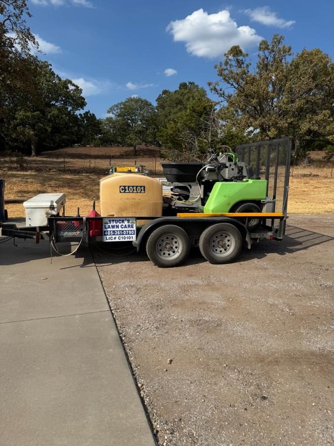 Side of the green Stuck's Lawn Care trailer, showing the tank and hose reel